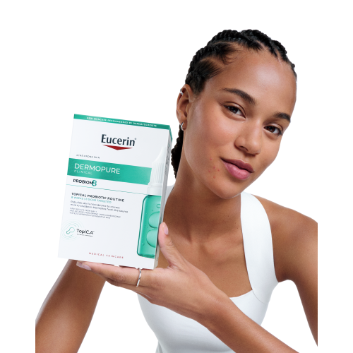 Eine junge Frau hält lächelnd eine Packung Eucerin Dermopure Clinical in die Kamera.